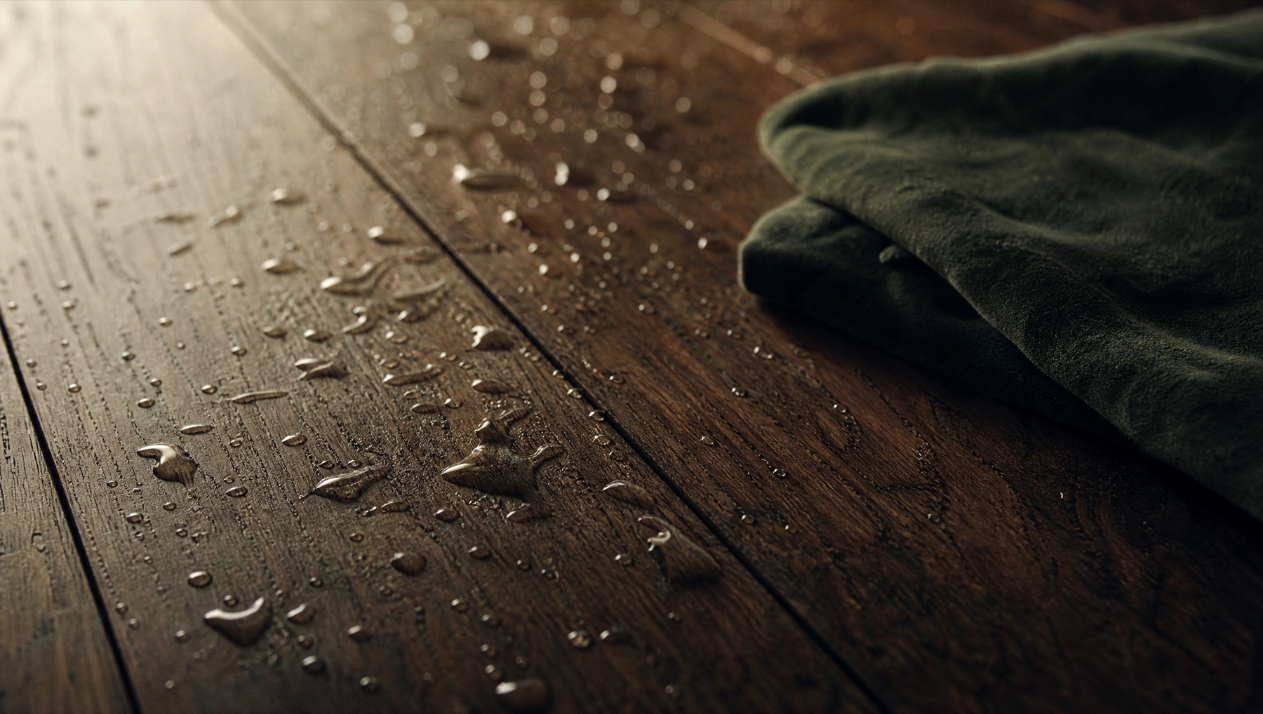 Water droplets beading on a dark finished hardwood floor beside a folded cloth