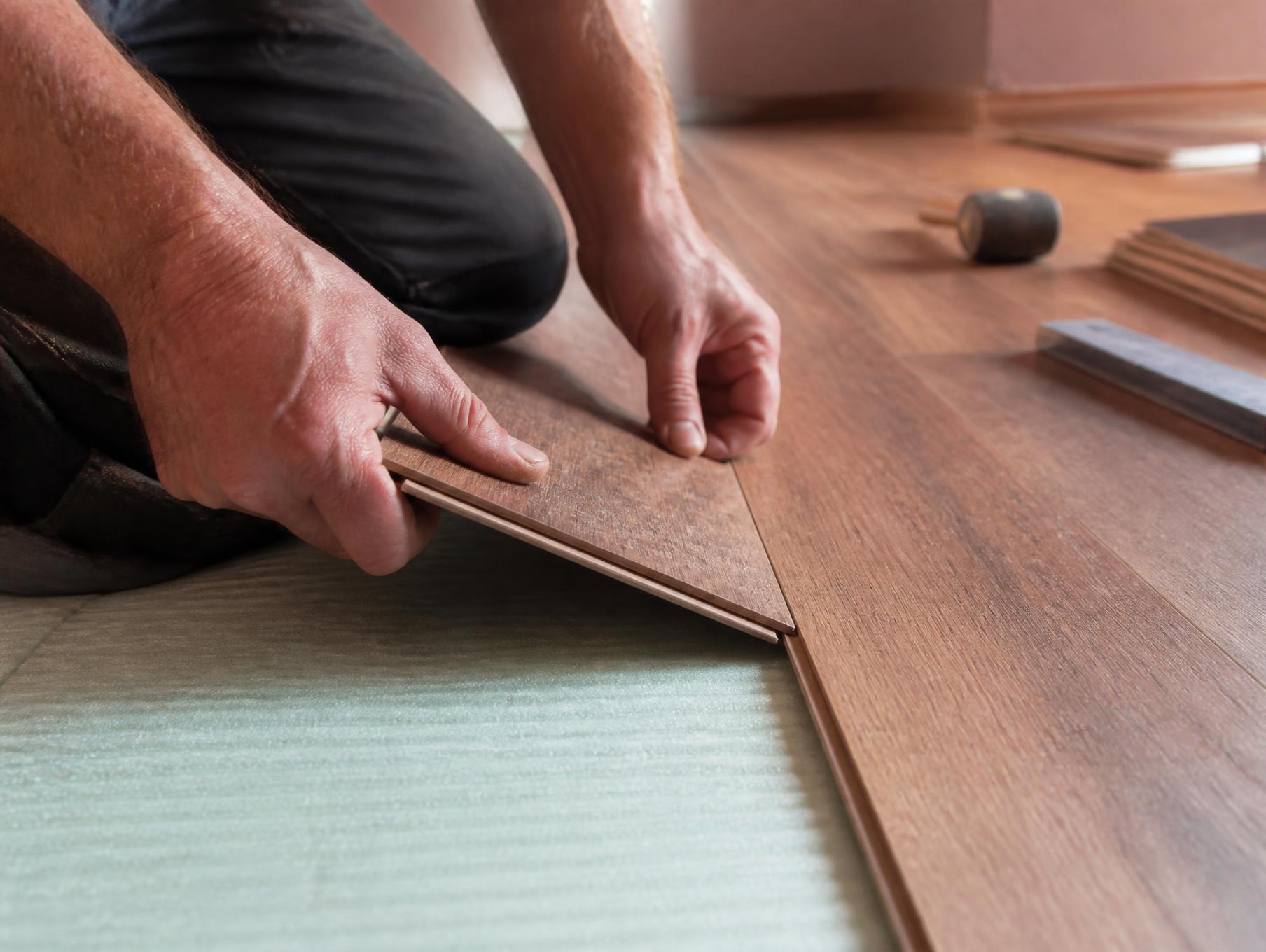 Installer clicking a laminate plank into place over foam underlayment