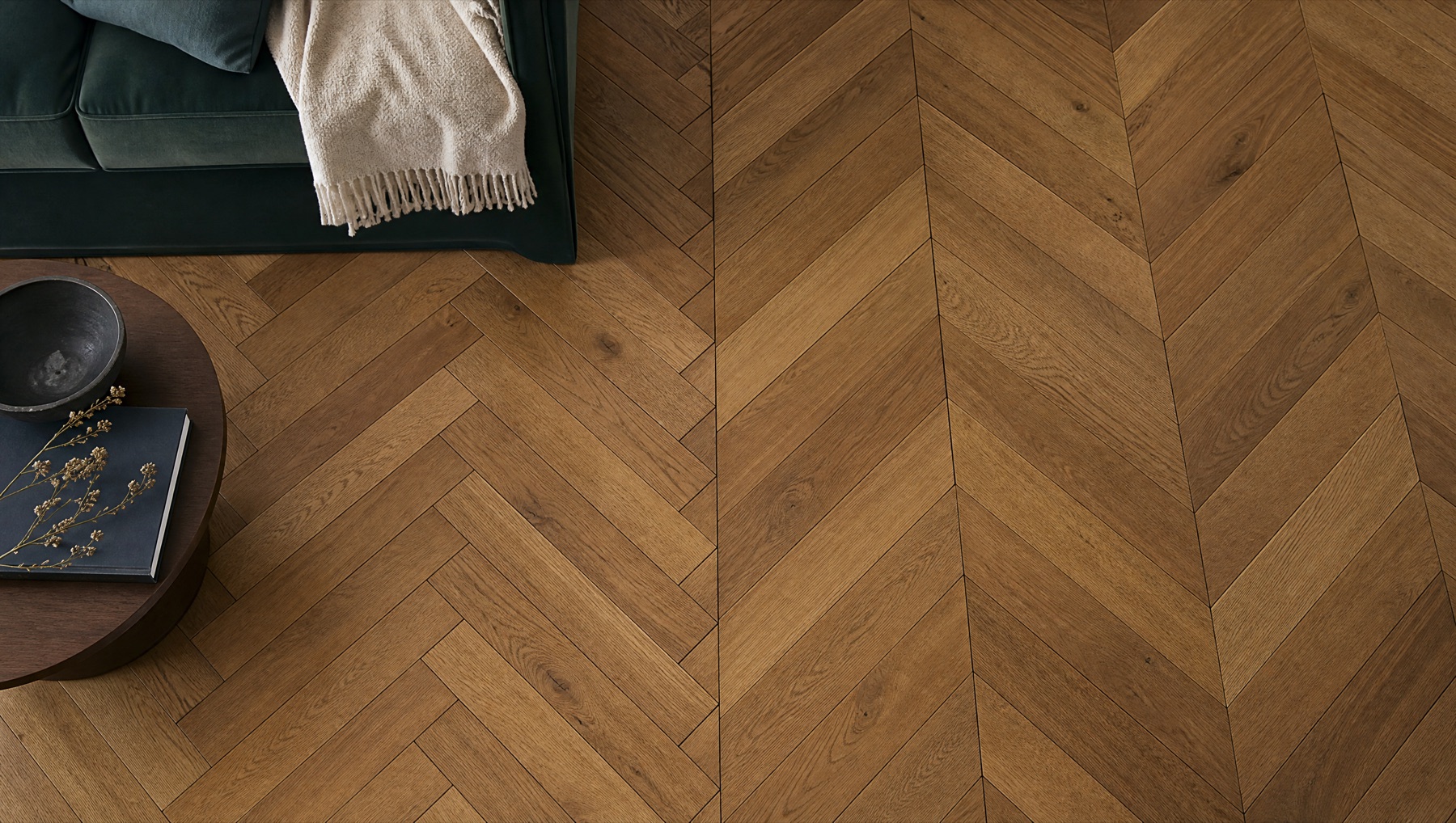 Close overhead view of warm oak chevron flooring beside a green sofa
